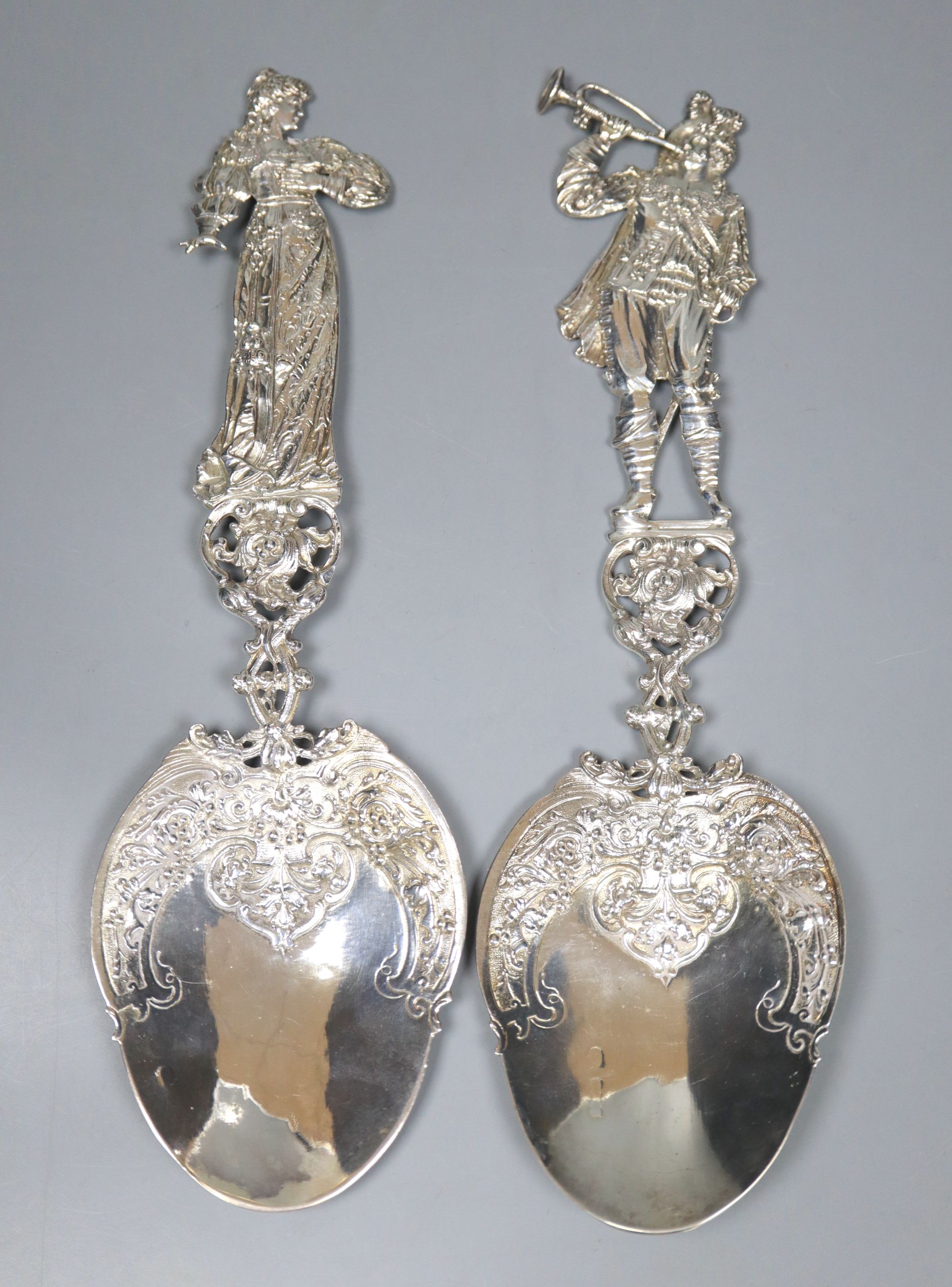 An ornate pair of late Victorian Hanau silver servers with figural handles, modelled as a lady and musician,